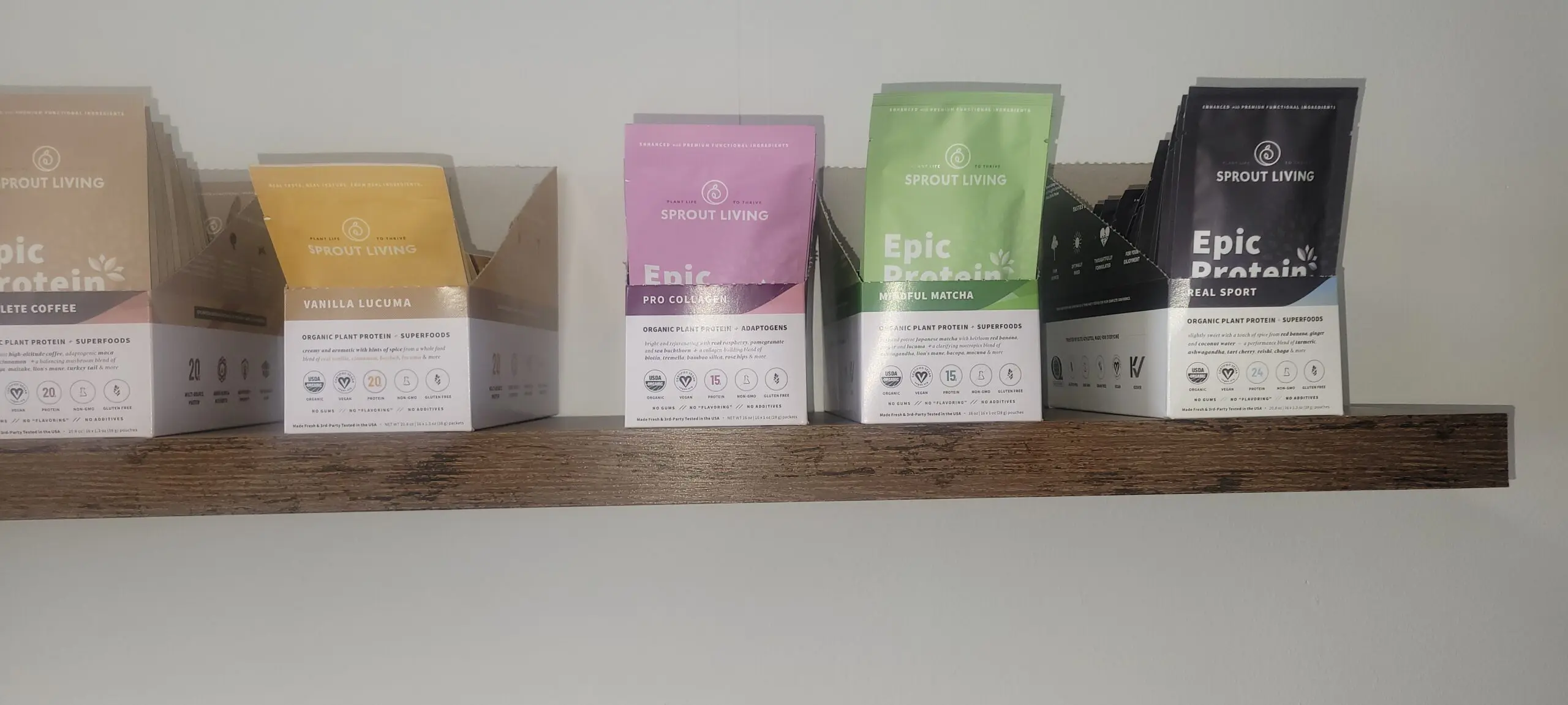 Four colorful tea packages displayed on a wooden shelf against a white wall.