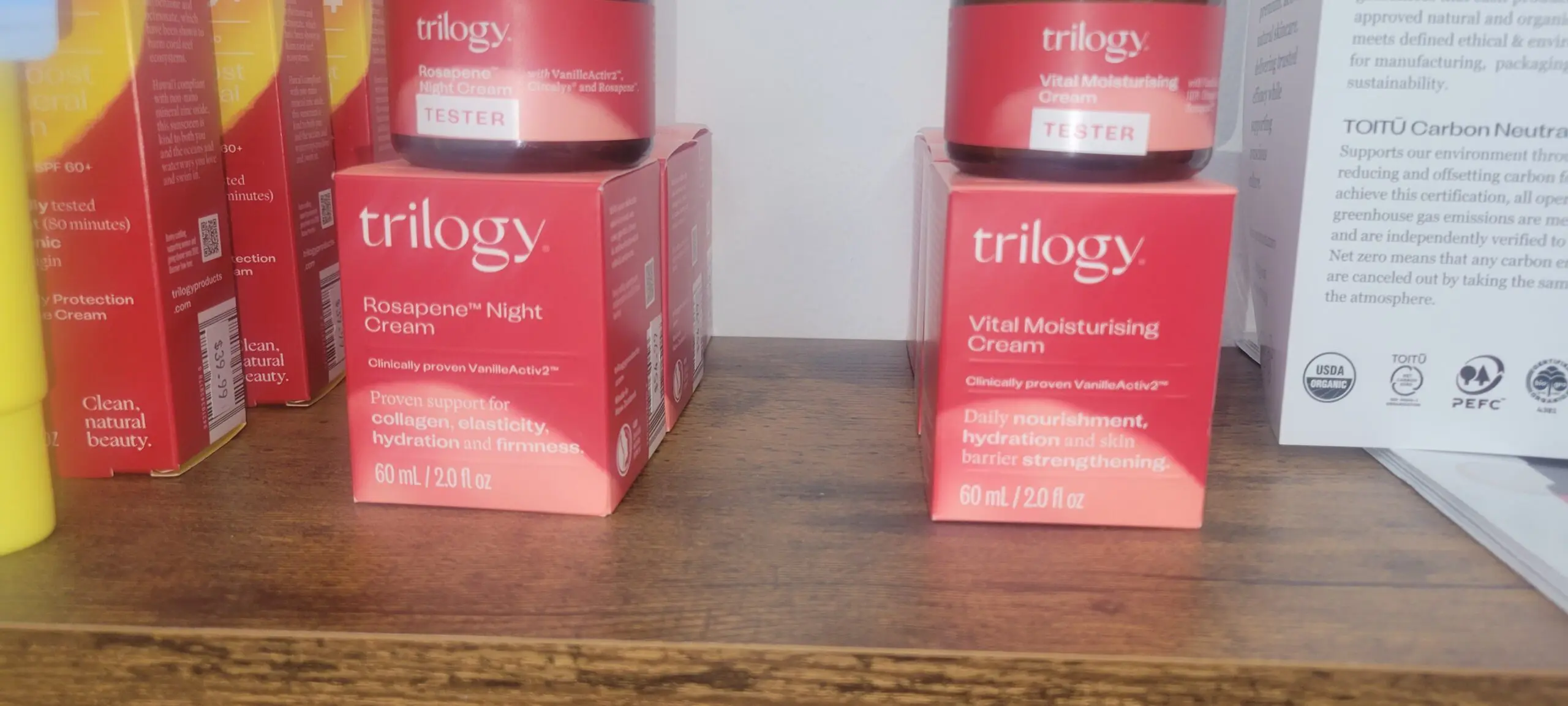 Two red Trilogy skincare product boxes on a wooden surface.