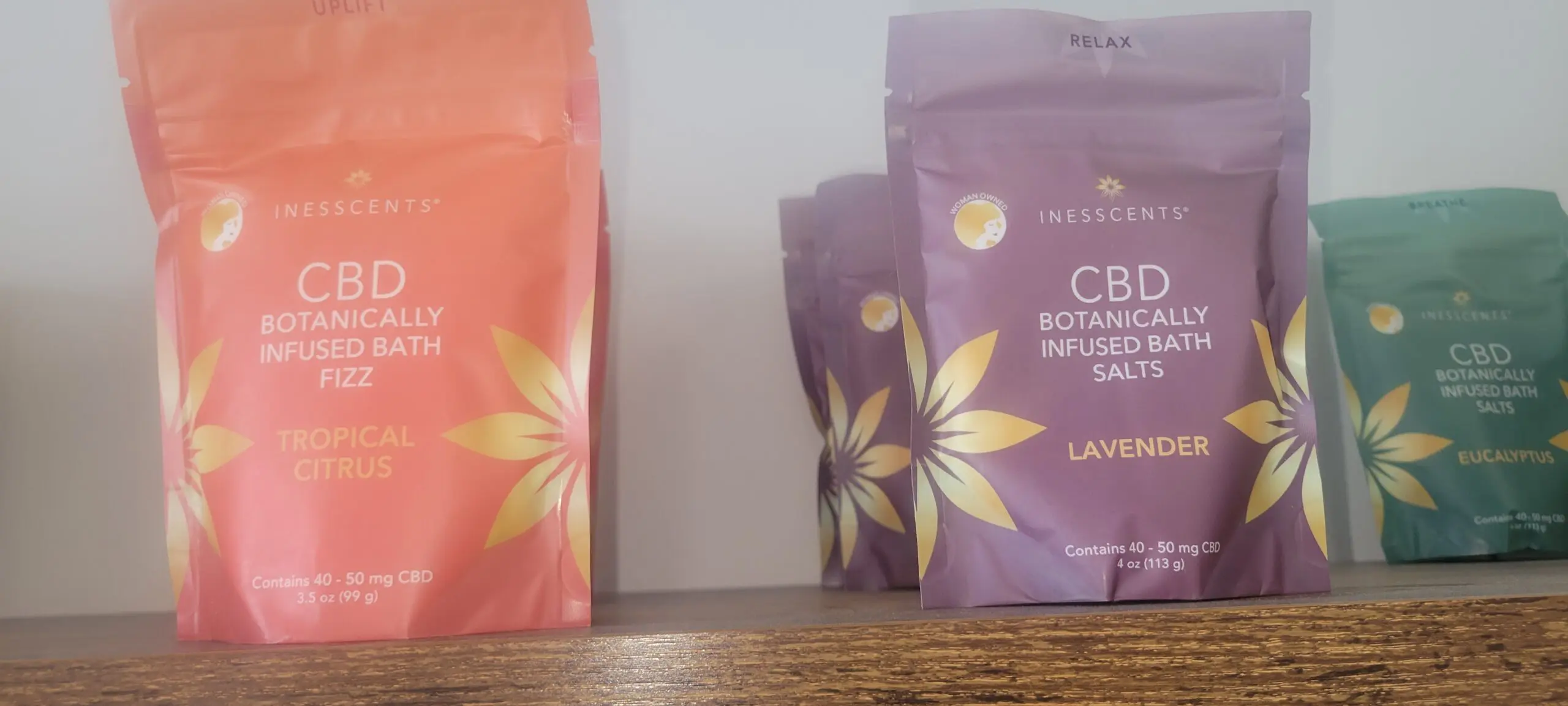 Two purple packets and one orange packet of botanical infusions on a wooden surface.