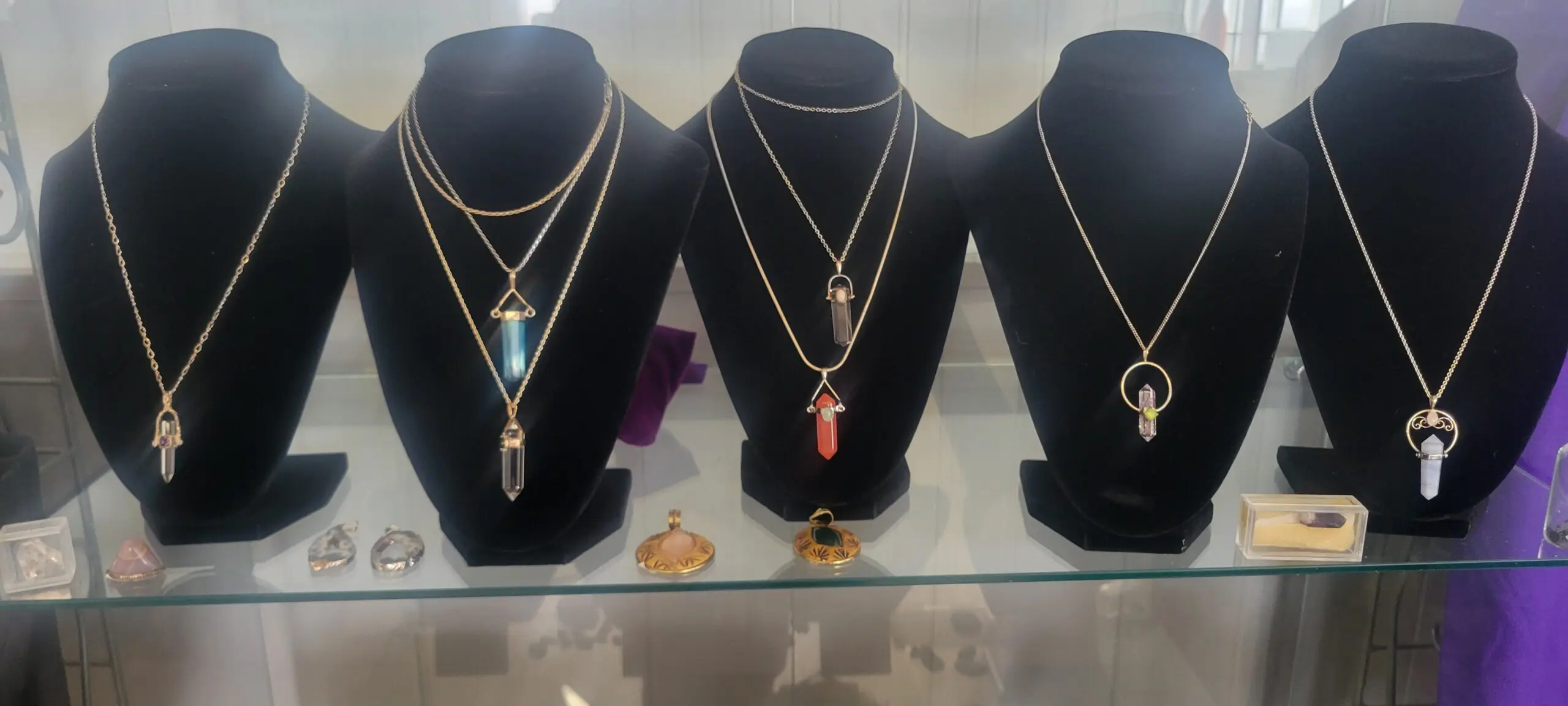 Display of elegant crystal pendant necklaces on black bust stands.
