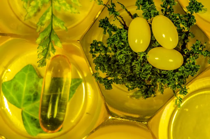 Yellow capsules and greenery on golden background.
