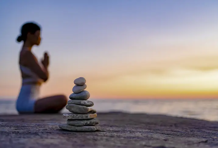 Person meditating with stacked stones at sunset.